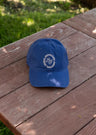 Blue Mountain Raised baseball cap with a white circular logo on the front resting on a wooden surface.